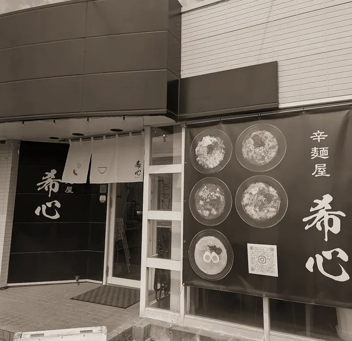 辛麺屋 希心の外観。黒い壁に白い筆文字の「希心」、白いのれん